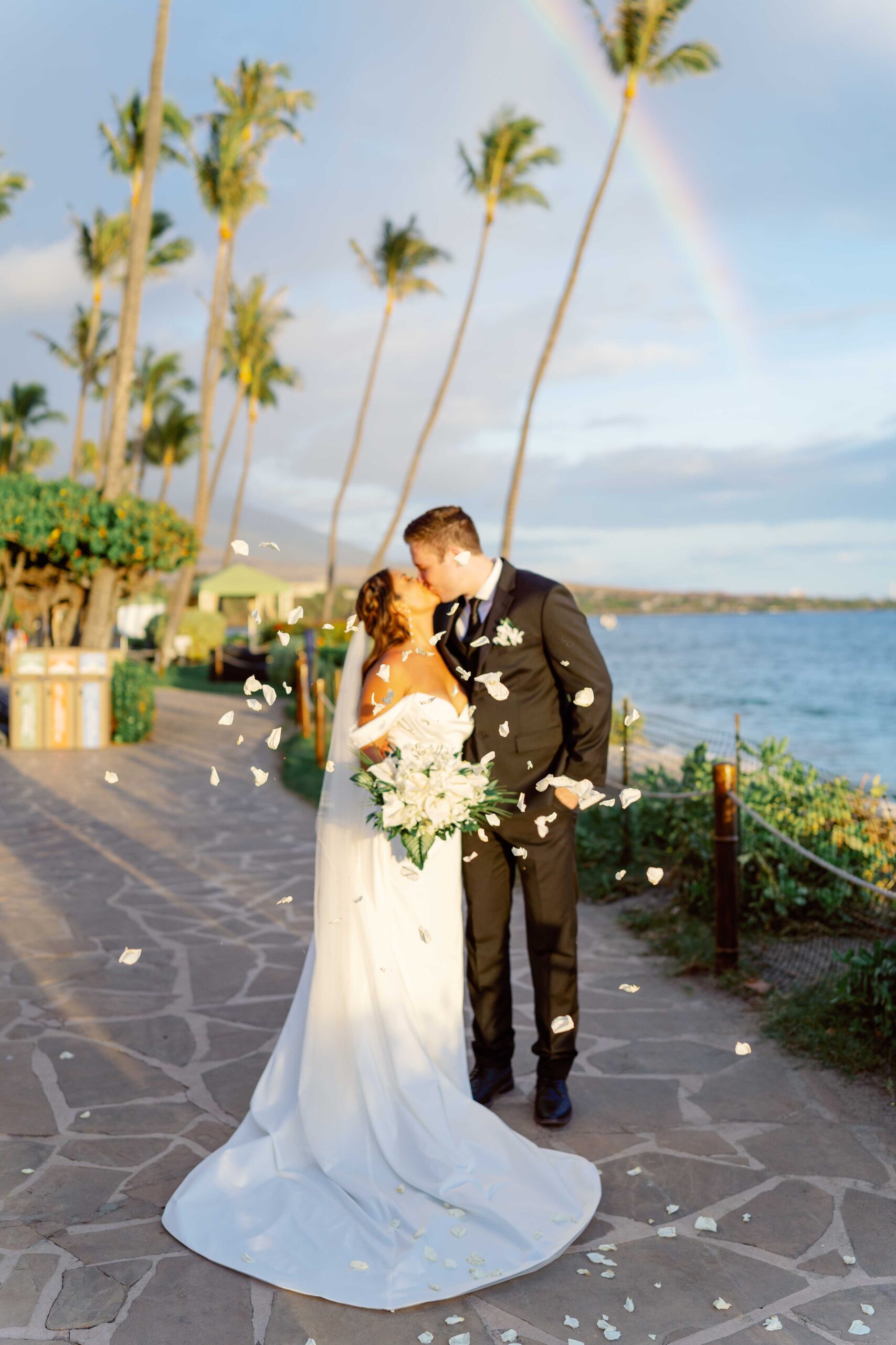 Bride and groom kissing on Maui with a rainbow behind them