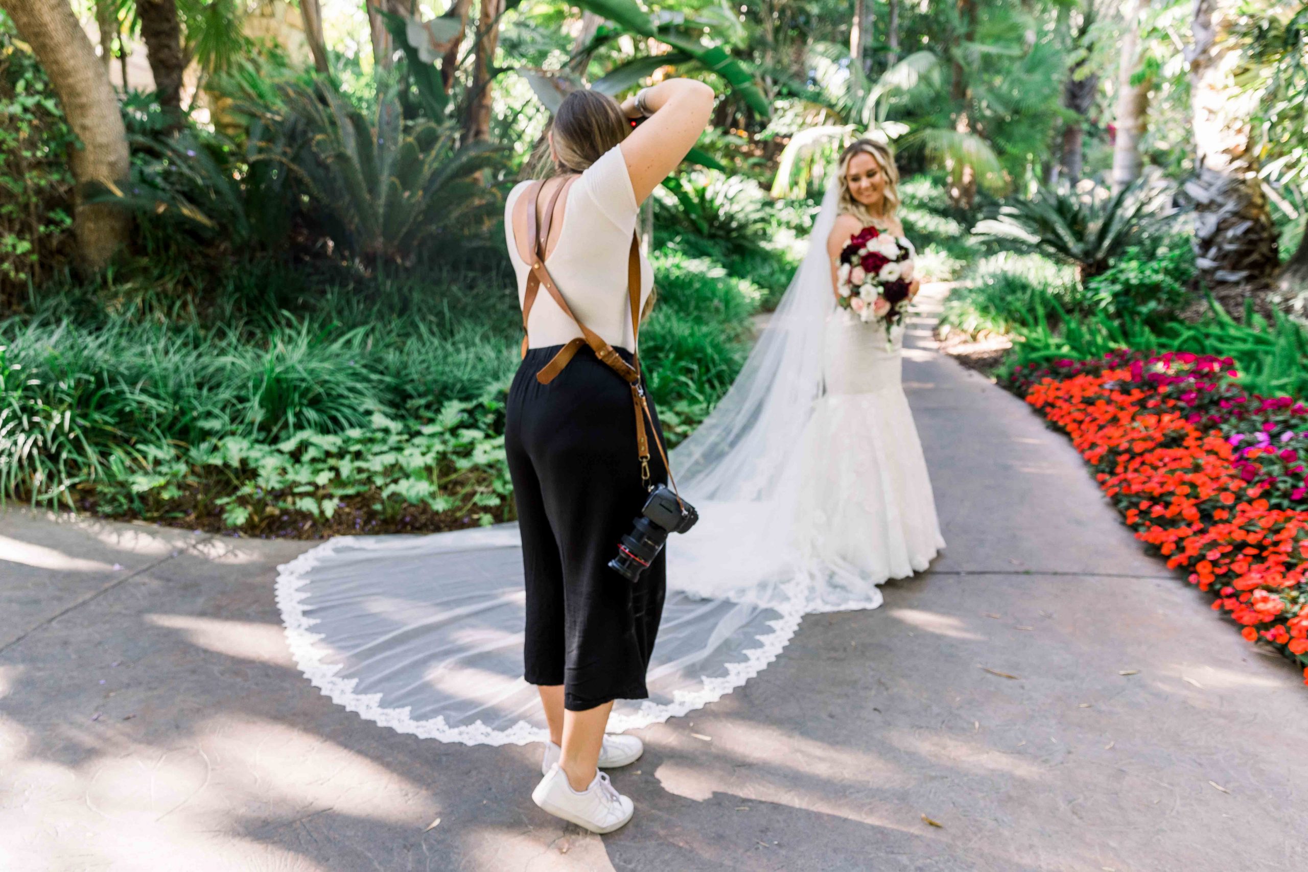 Woman photographer with camera harness taking a photo of a bride with long veil