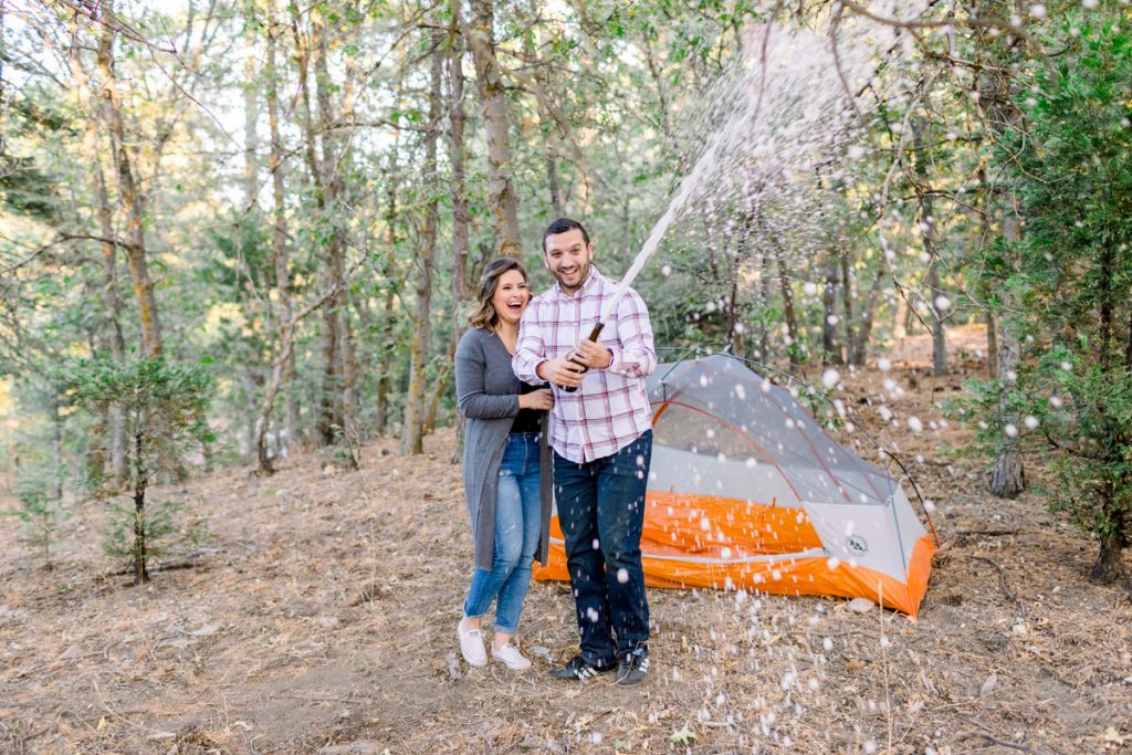 Couple popping champagne in forest by orange tent