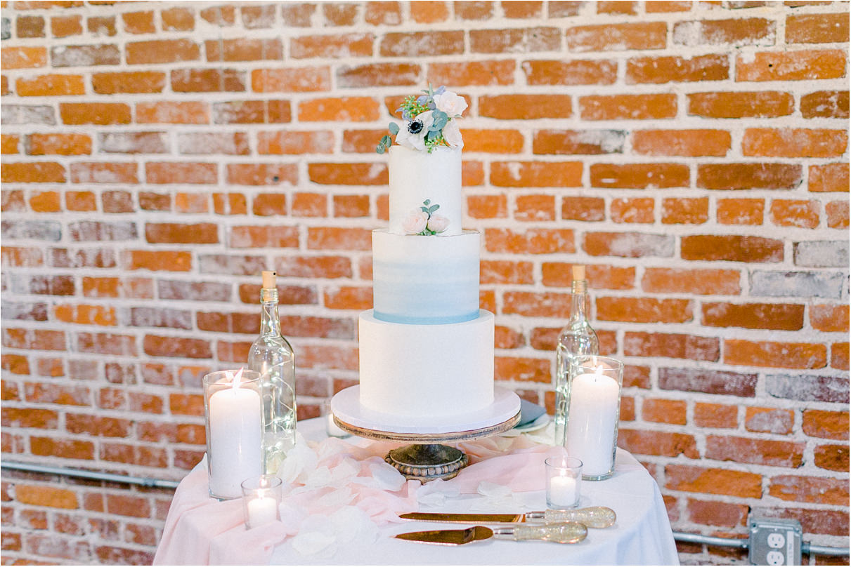light blue wedding cake on table with candles against brick wall
