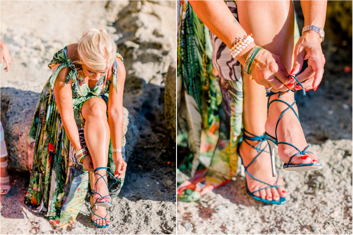 Woman in colorful dress putting on strappy turquoise heels at beach