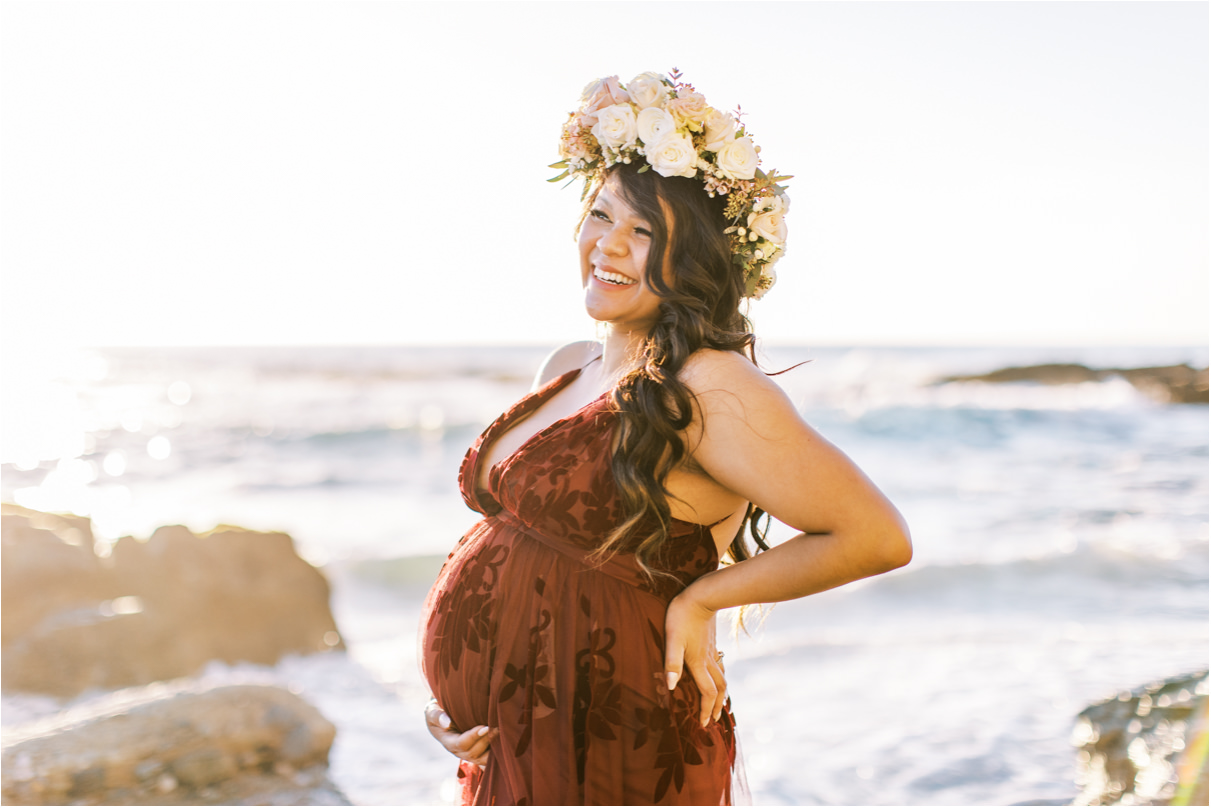 Pregnant woman in maroon dress and rose flower crown at the beach