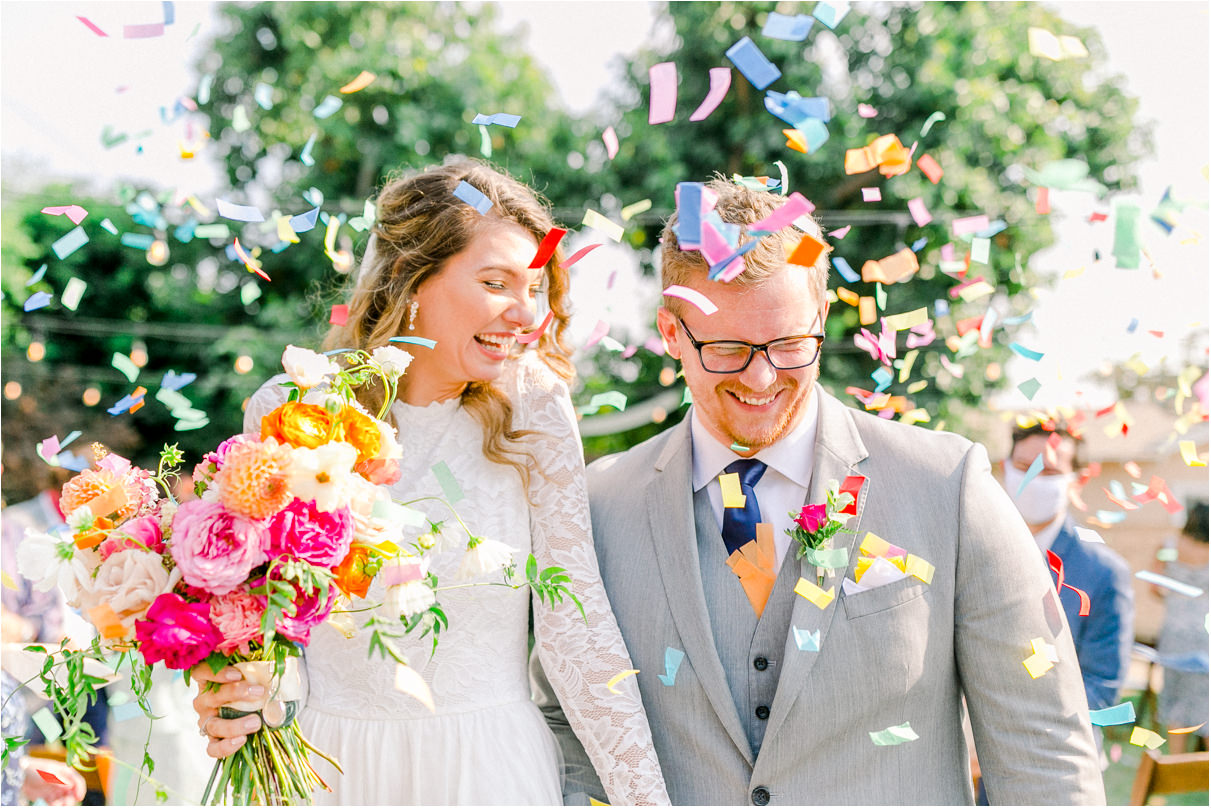 Bride and groom walking down aisle with large colorful confetti falling around them