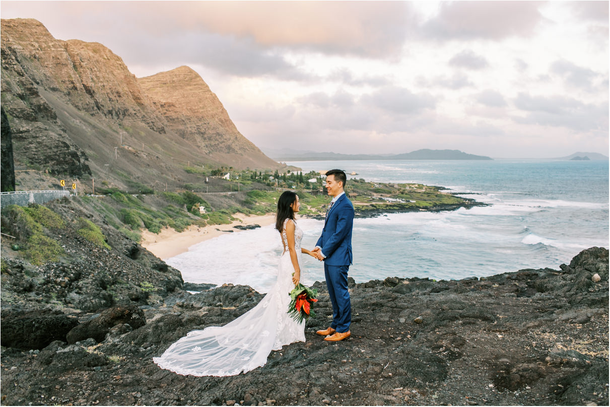 Bride and groom holding hands overlooking beach in hawaii