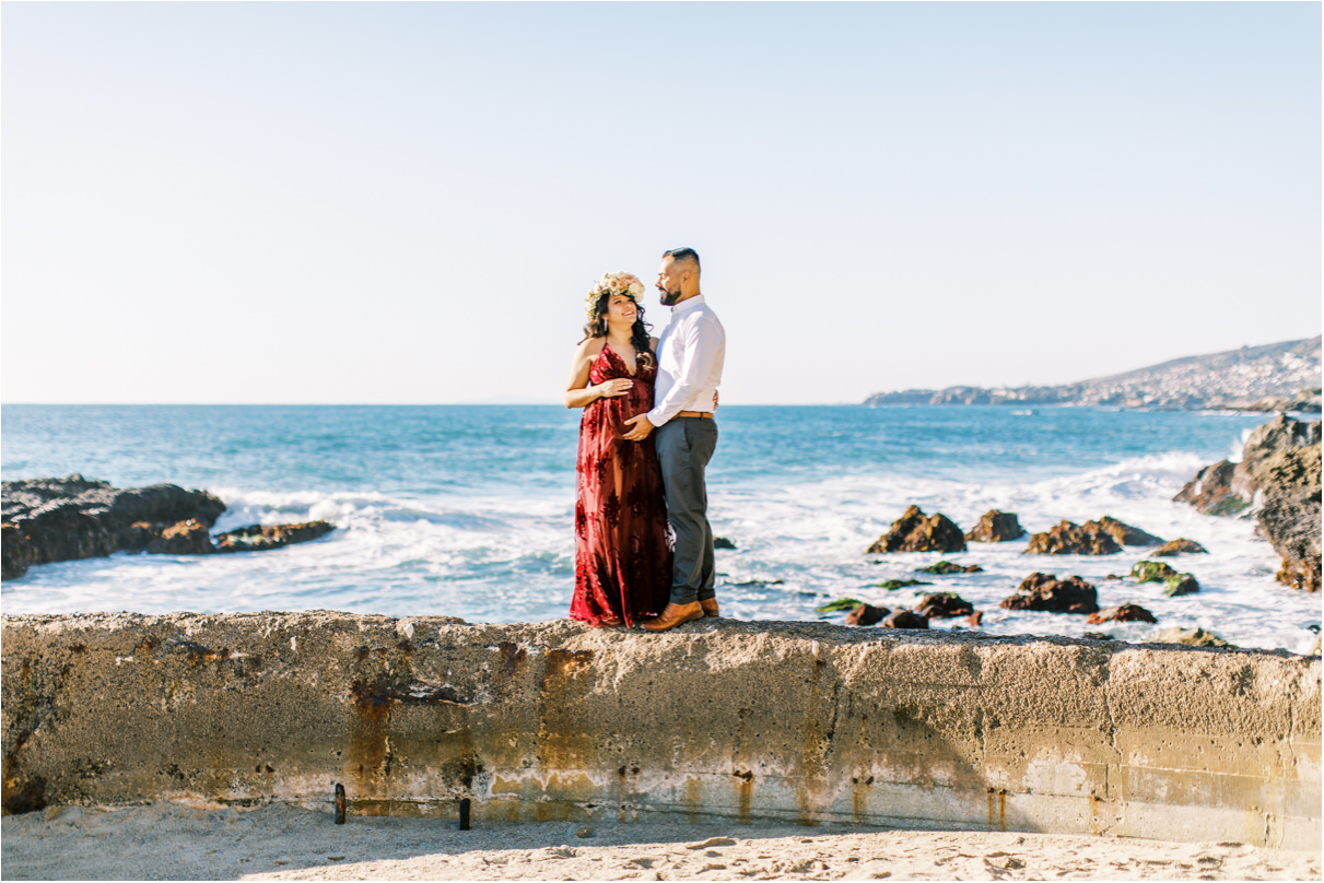 Pregnant woman with husband standing on sea wall at beach