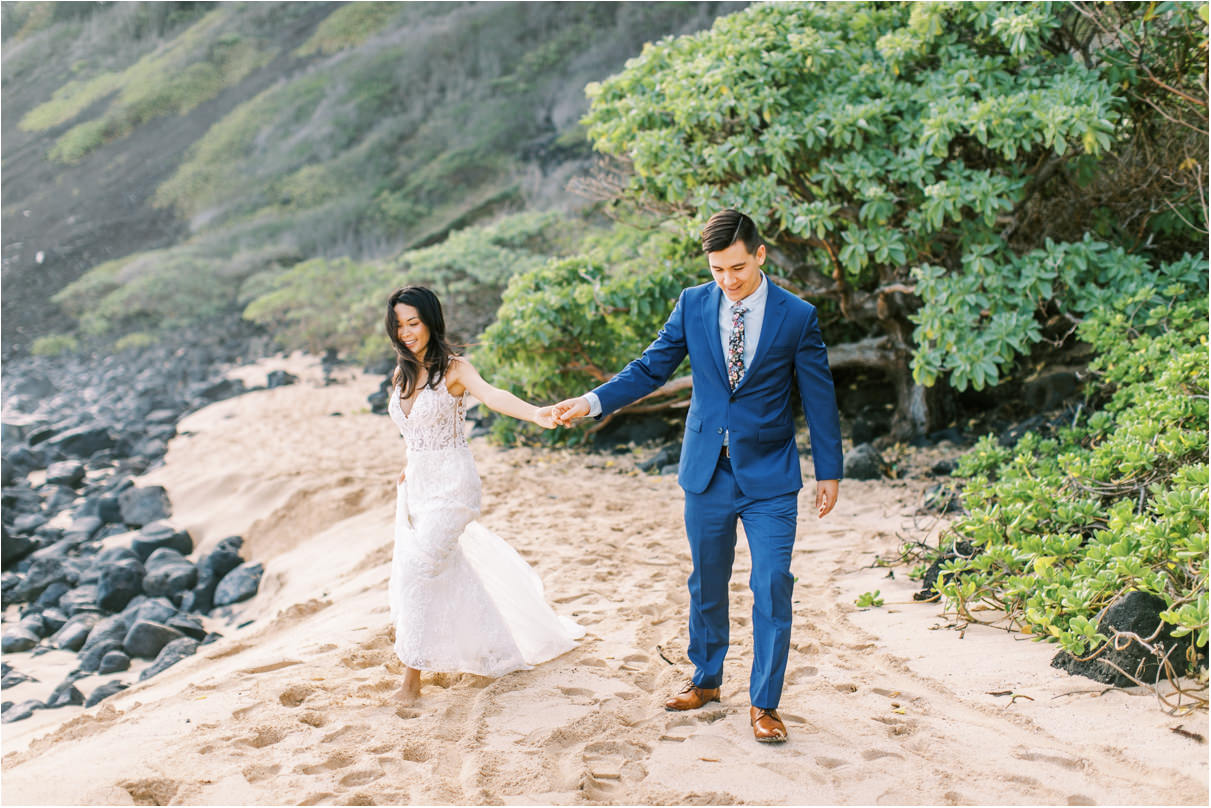 Wedding couple holding hands and walking towards camera on the sand