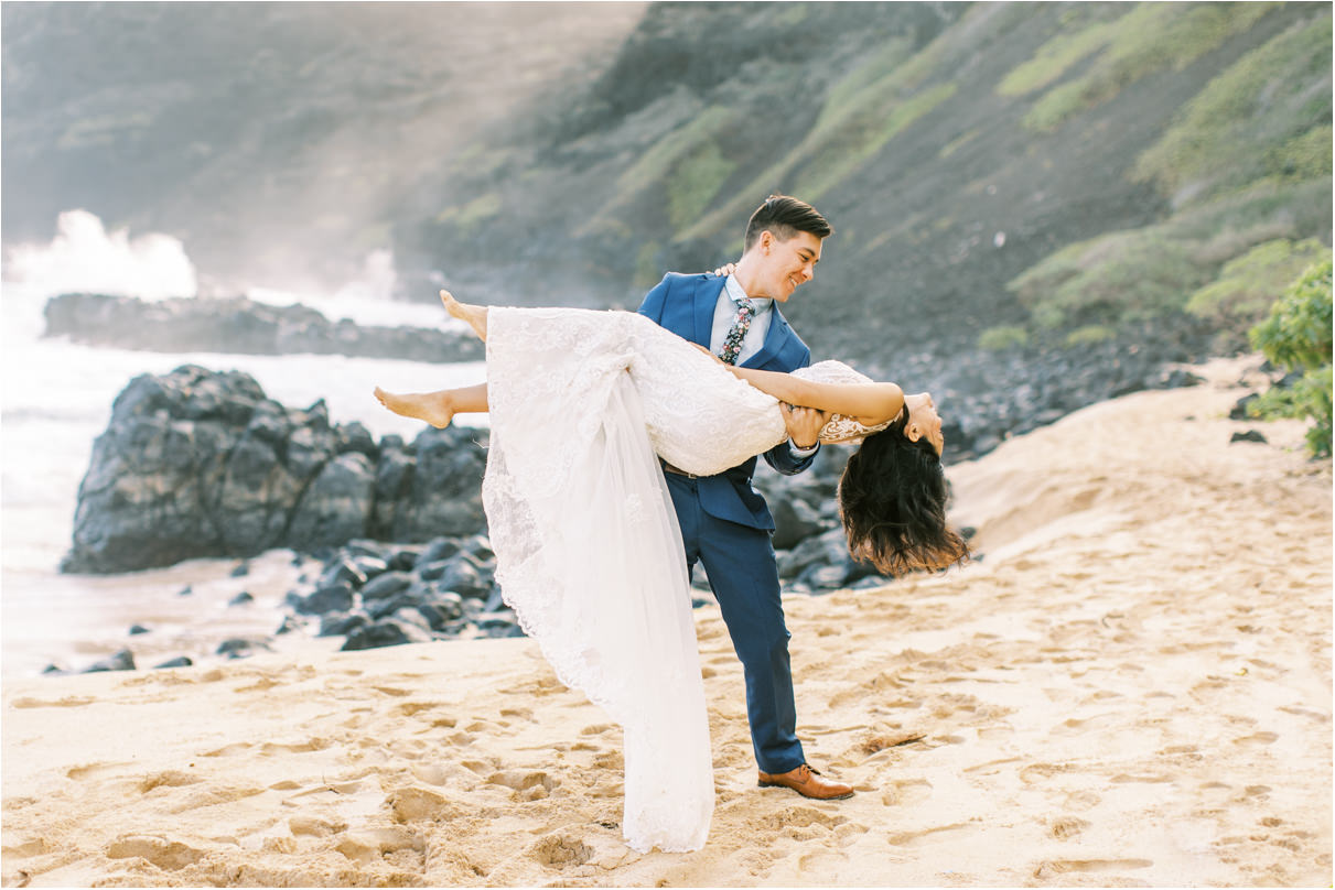 Groom carrying bride on beach with long wedding train