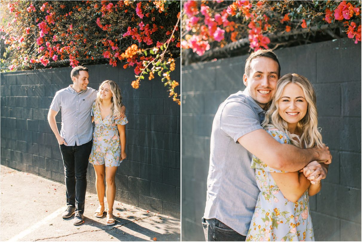 Engaged couple hugging against black brick wall with red flowers 