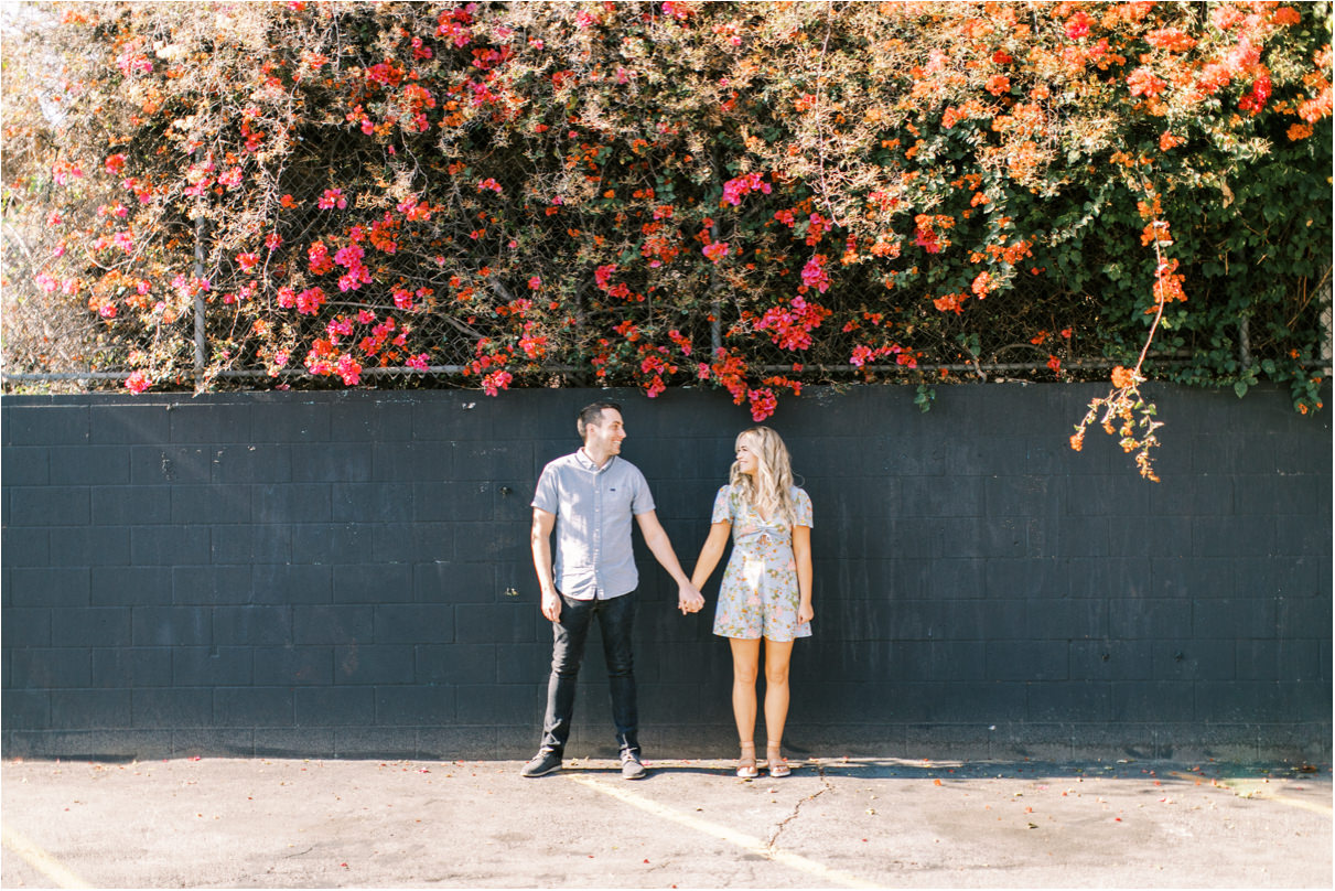 Couple holding hands against black wall with flowers above them