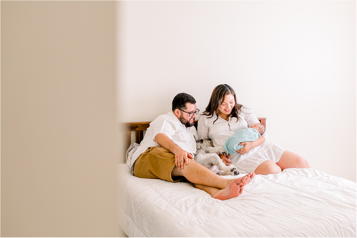 Viewer is peeking into bedroom as mom, dad, and dog are looking at newborn baby.