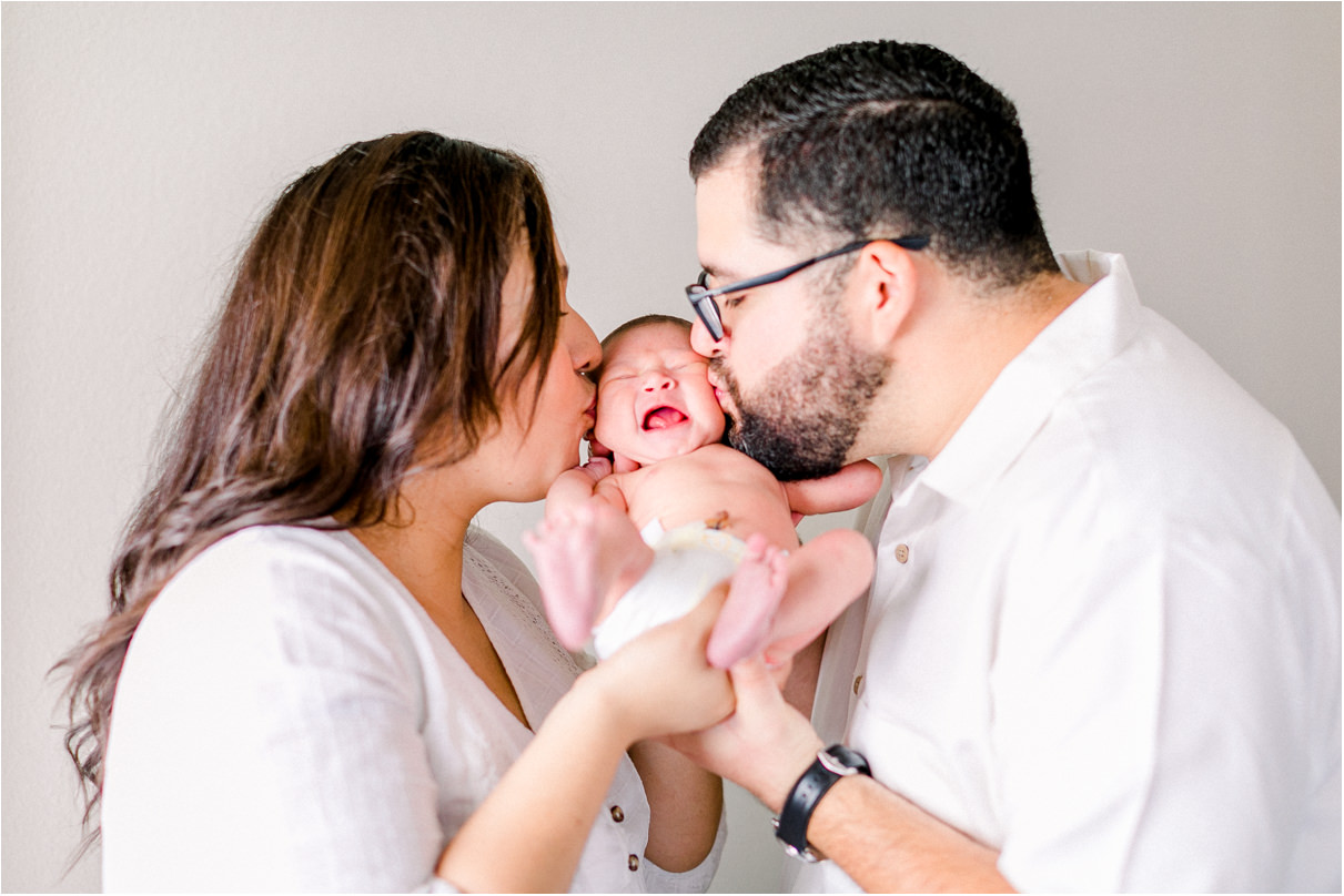 Mom and Dad kissing newborn baby boy on either side of this face and baby is crying