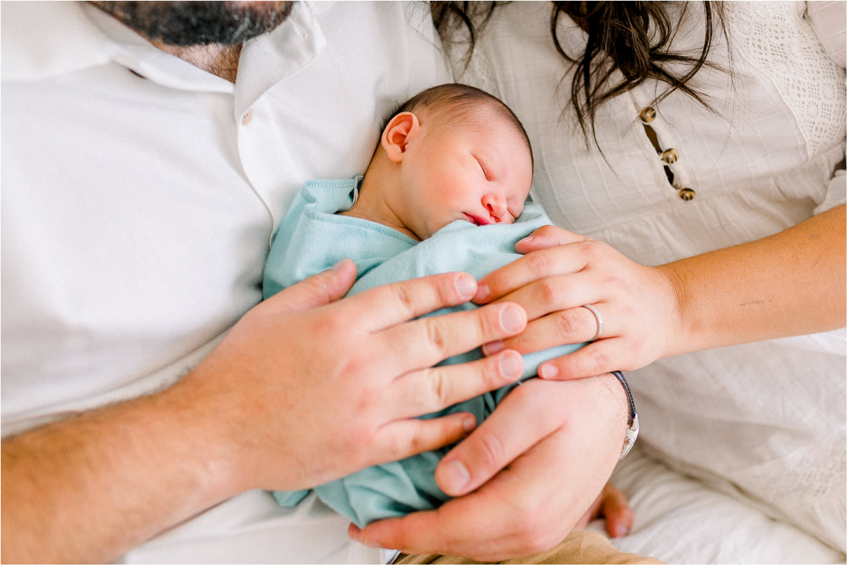 Parents are holding sleeping newborn sleeping baby in turquoise swaddle