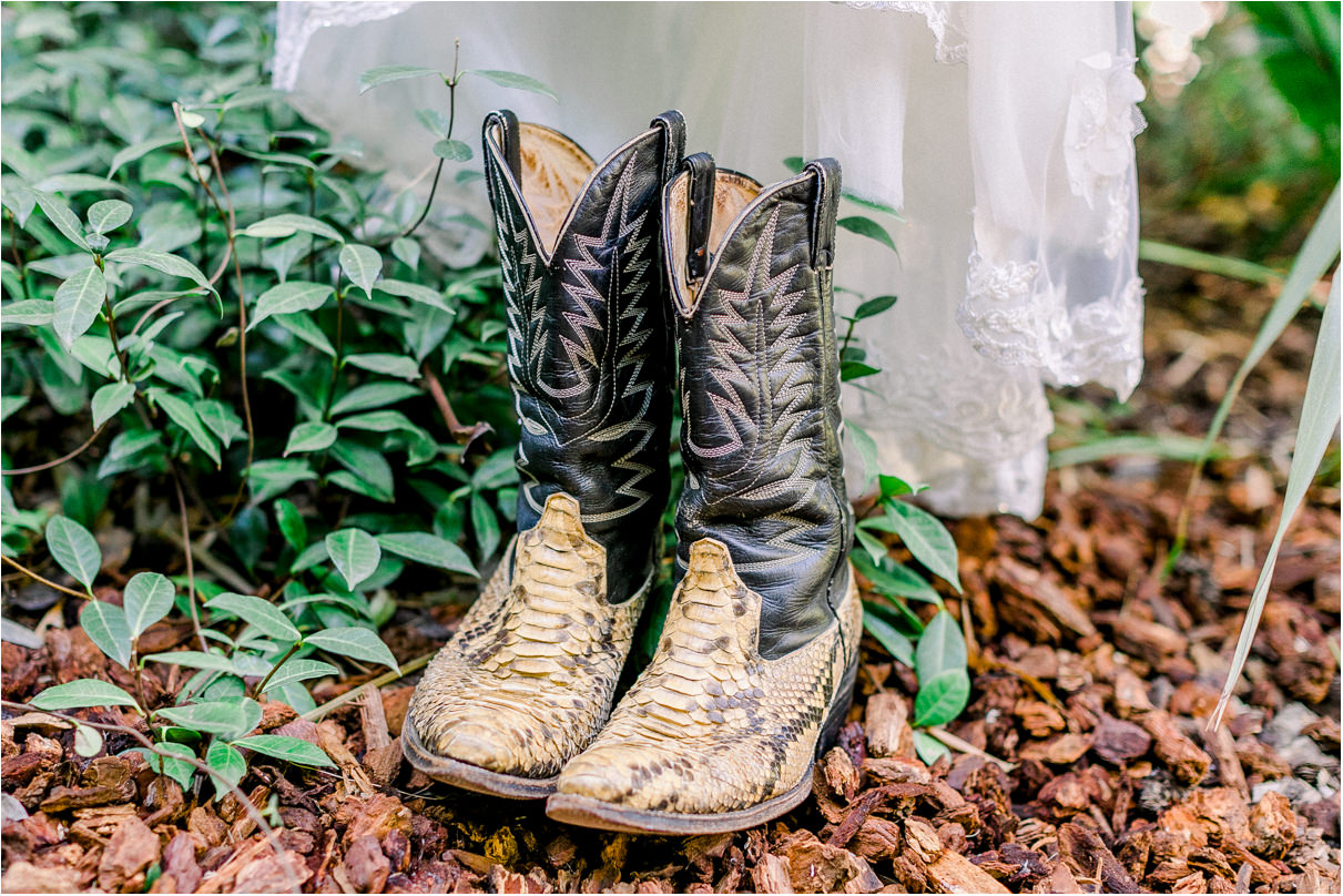 Men's cowboy boots sitting below wedding dress in flower bed