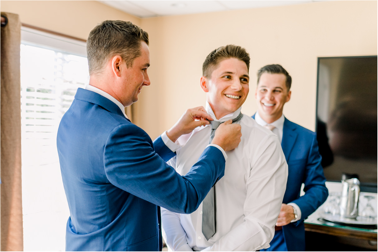 Groom smiling as brother helps him adjust his tie