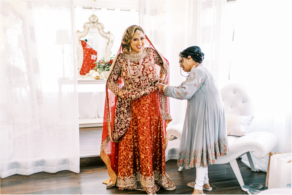 Pakistani bride with mom helping her put on intricate red skirt