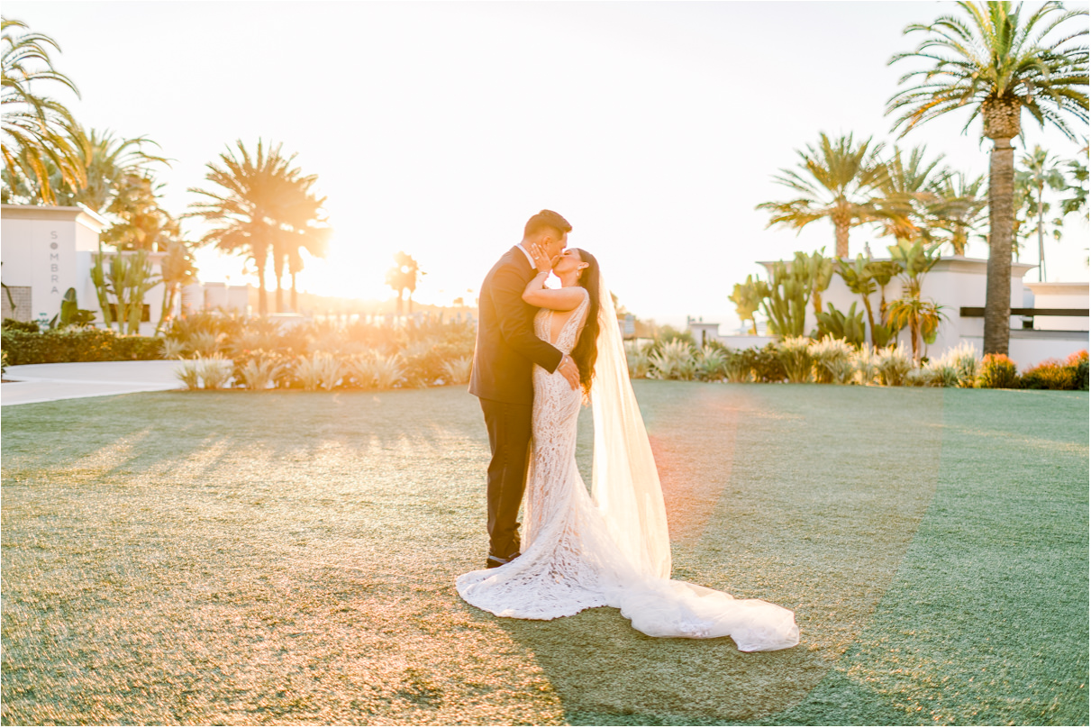 Bride and groom kissing on lawn at sunset