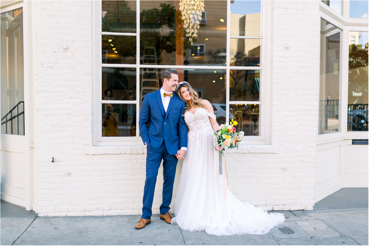 Bride and Groom holding hands smiling outside white brick building in San Diego