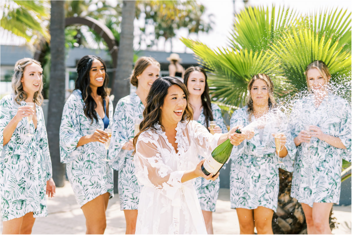 Bride popping champagne on beach with bridesmaids