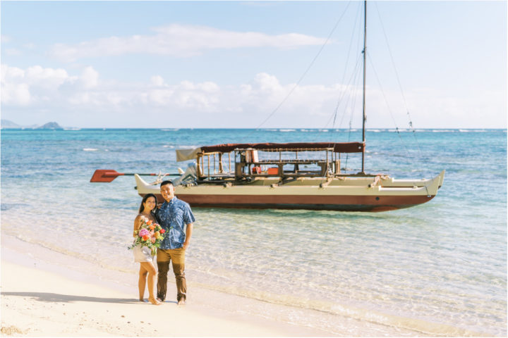 Couple standing in ocean with catamaran boat