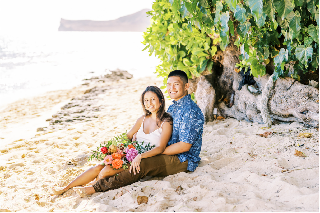 Couple sitting in sand for engagement session in hawaii