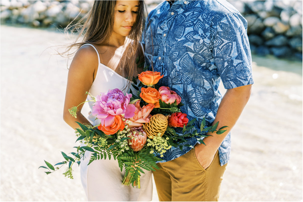 Couple at the beach holding tropical bouquet for engagement photos in hawaii