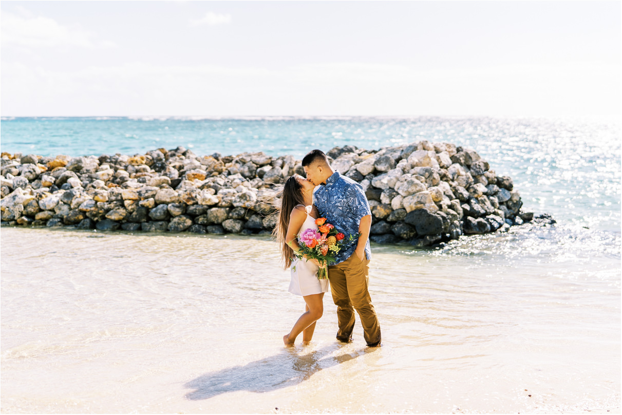 couple kissing in ocean water with rock wall behind them