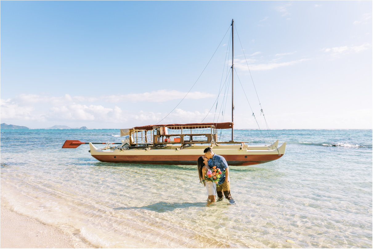 Couple standing in ocean water in front of large catamaran boat kissing