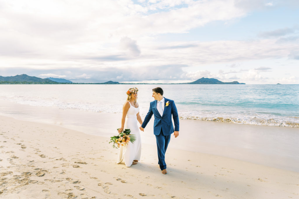 Bride and groom holding hands walking along oahu beach