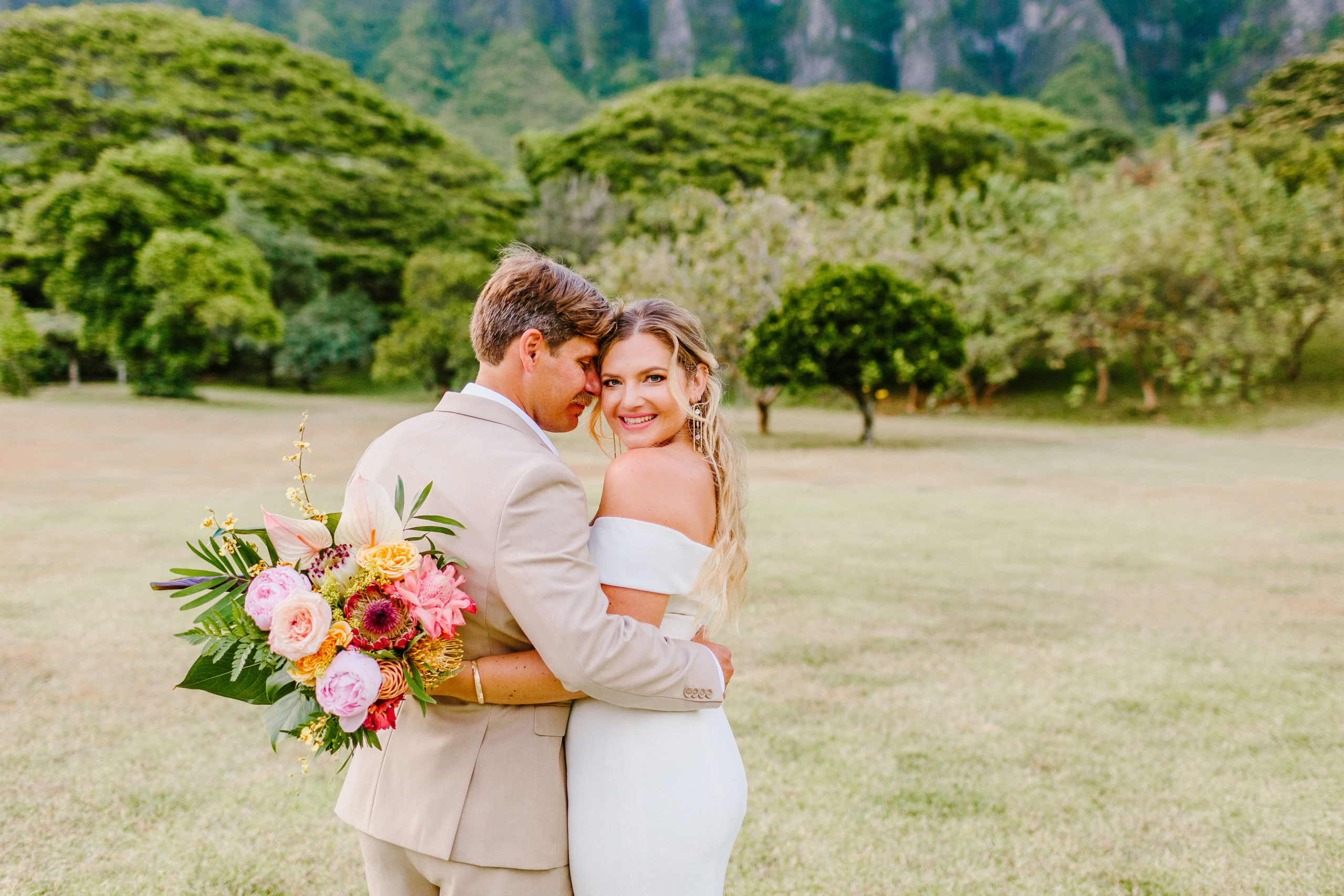 Bride and groom snuggling holding tropical bouquet