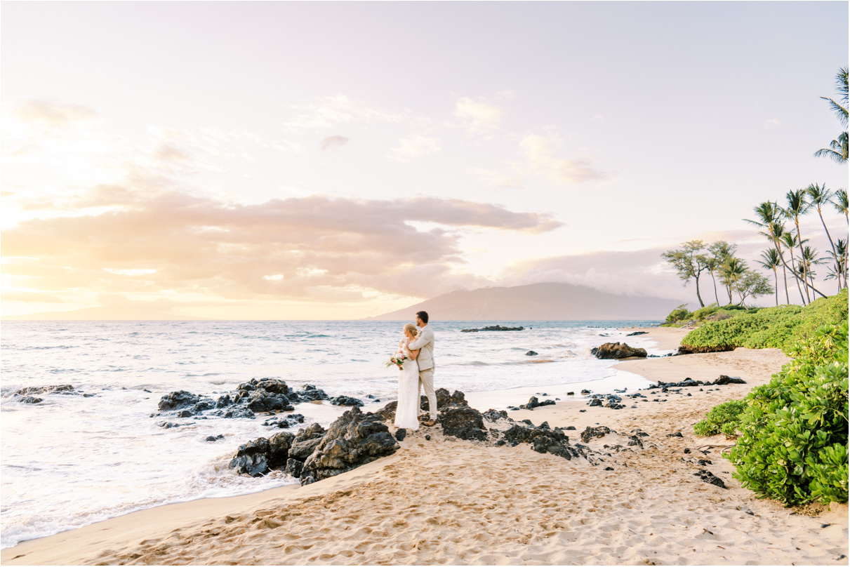 wide landscape photo of bride and groom looking out towards sunset on the beach in Maui