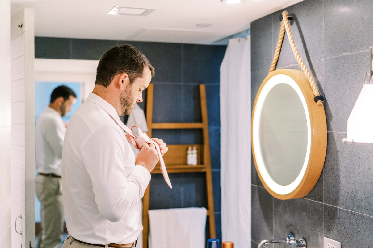 groom putting on tie in hotel bathroom