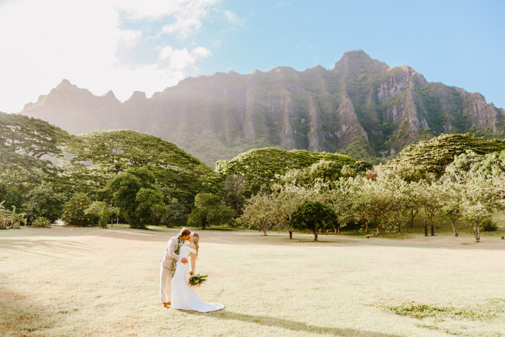Bride and groom kissing on oahu in front of tall mountain range