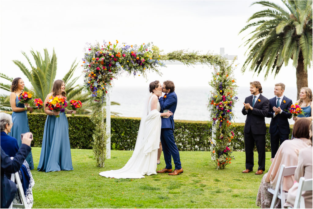 bride and groom first kiss under floral arch